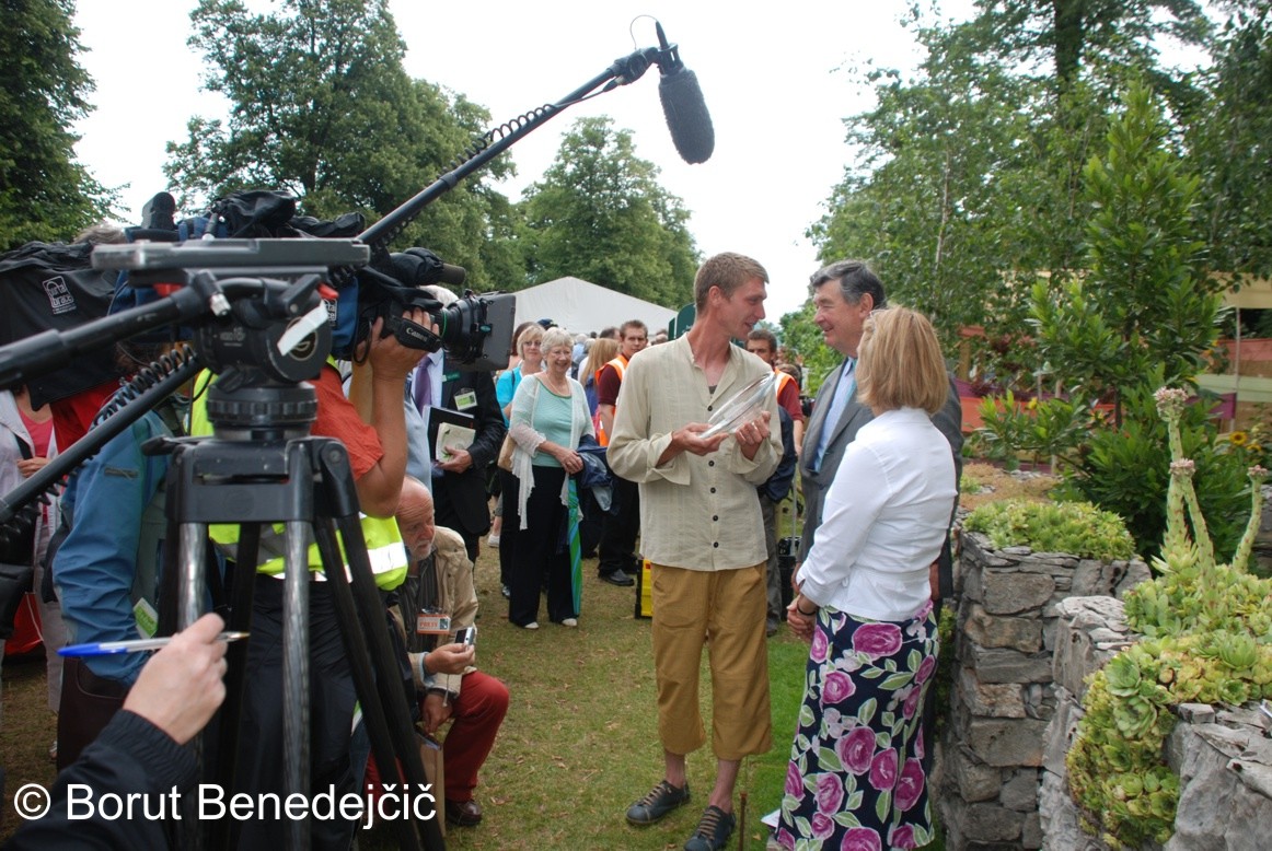 Avtor kraškega vrta v družbi predstavnikov Kraljevega hortikulturnega društva, ki sta mu predala odličja in seveda v soju kamer in mikrofonov.
